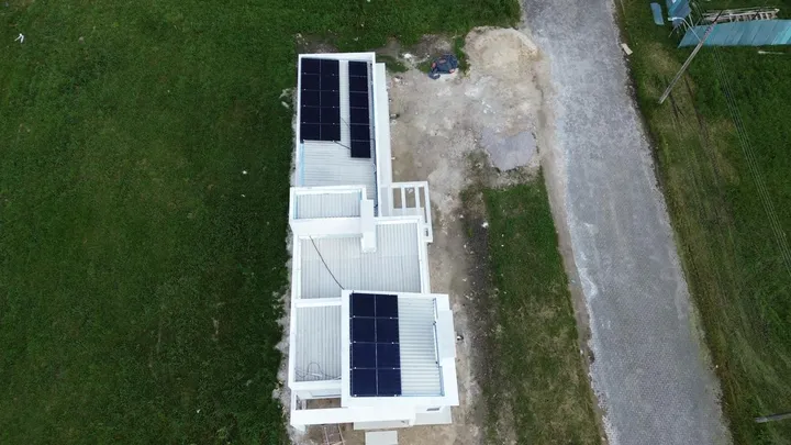 Vista aérea de edificação com módulos fotovoltaicos em dois níveis de laje, cercada por gramado